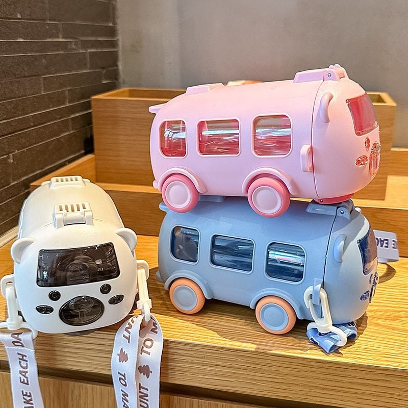 Three water bottle & toy buses, one pink, one white and one blue, on a wooden surface with a neutral background.