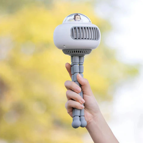 Hand holding a gray handheld fan with a blurred outdoor background