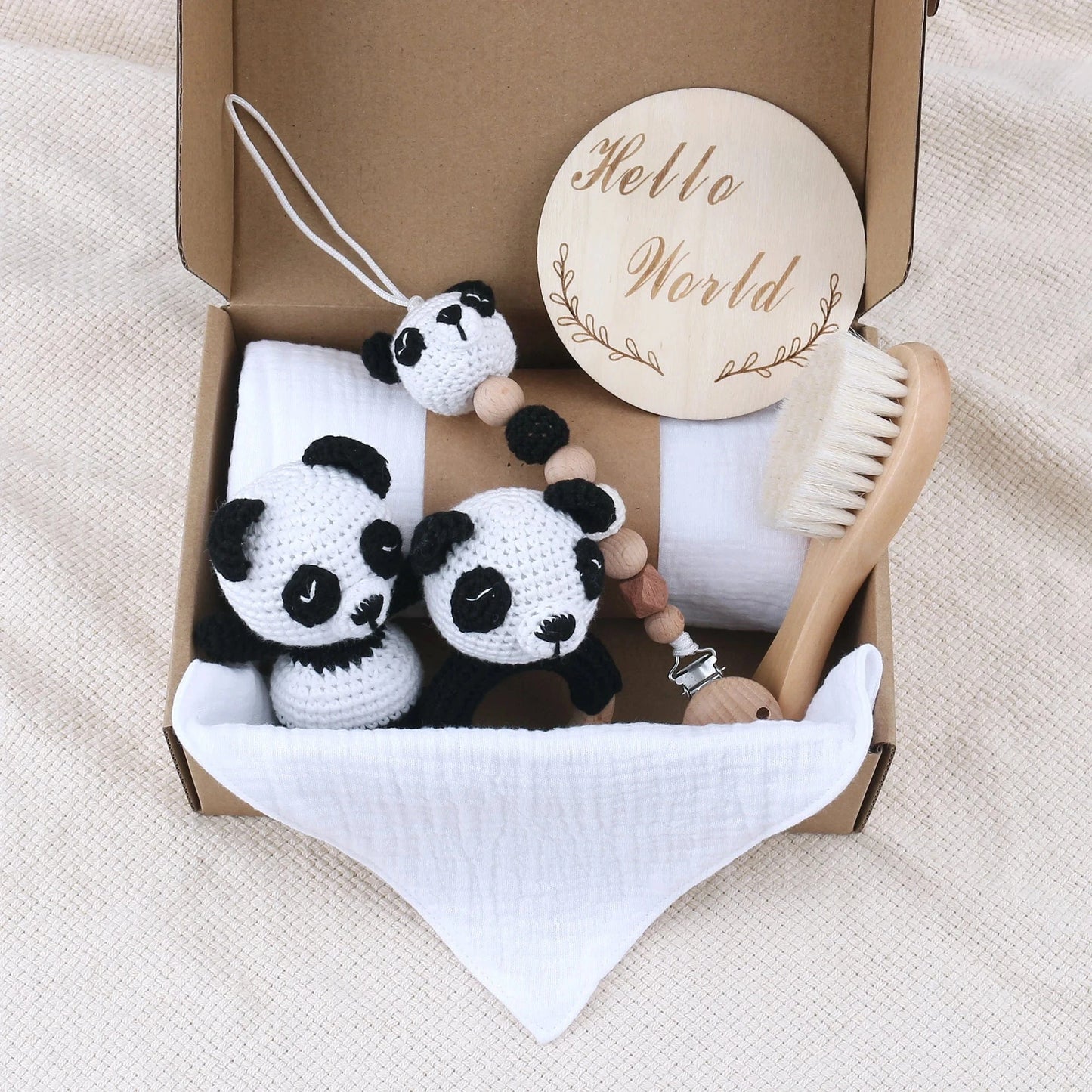 Baby care items including panda toys, a wooden rattle, and a brush in a box on a beige blanket.