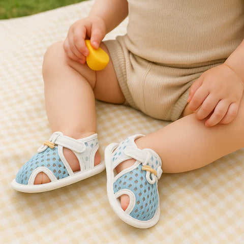 Baby wearing blue sandals with white soles on a checkered blanket.
