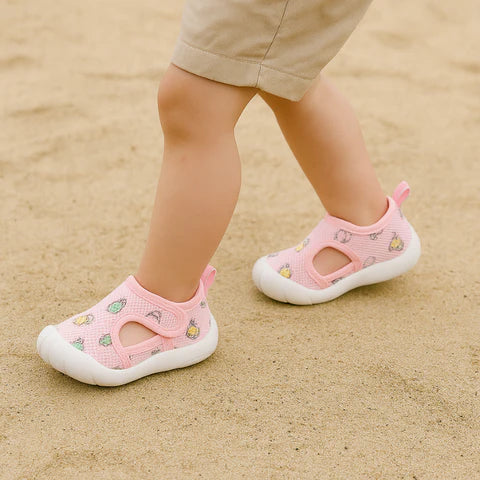 Child wearing pink sandals with white soles on a sandy surface