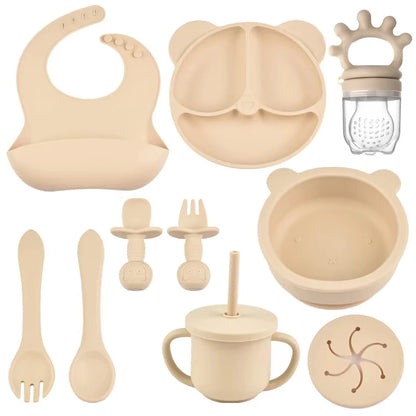 Collection of beige baby feeding and utensil items including a bib, bowl, cup, and various tools on a white background.