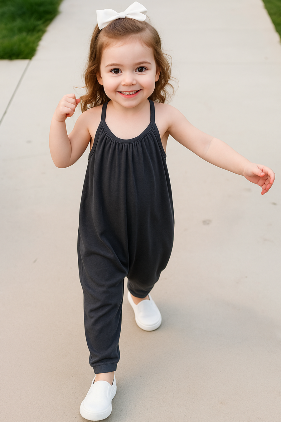 Child wearing a black romper with a white bow in their hair, standing on a sidewalk.