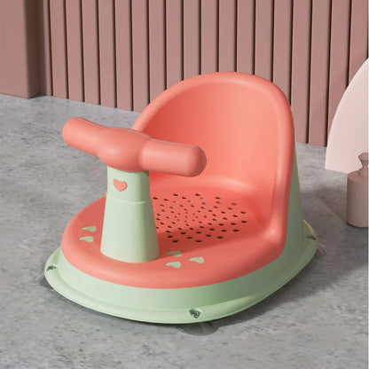 Children's training seat with pink seat and green base on a gray surface.