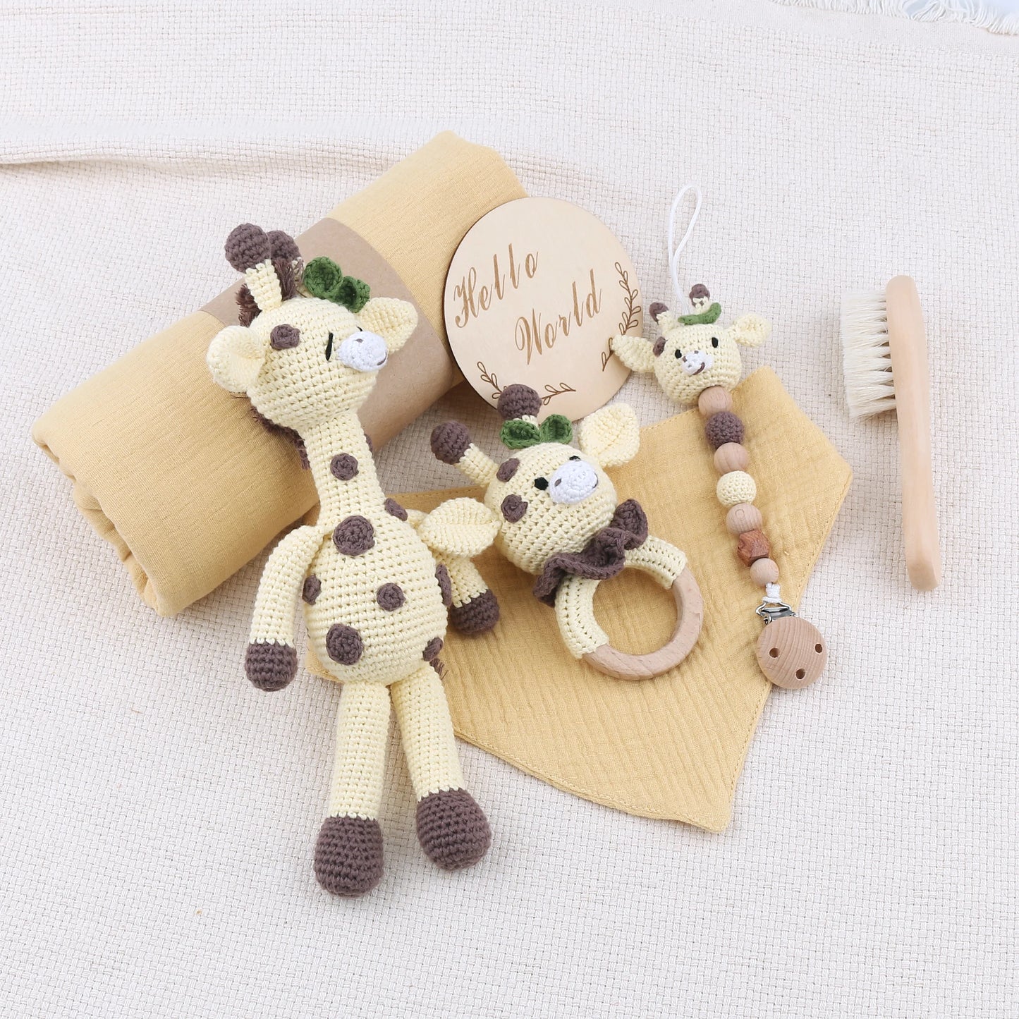 Set of baby toys including a crocheted giraffe, teething ring, and brush on a white background.