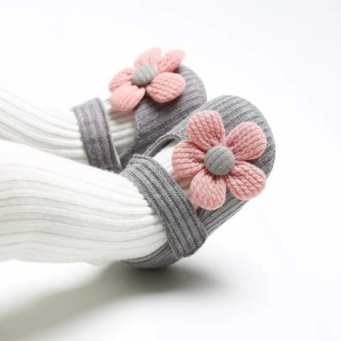 Pair of gray and white slippers with pink flower decorations on a white background