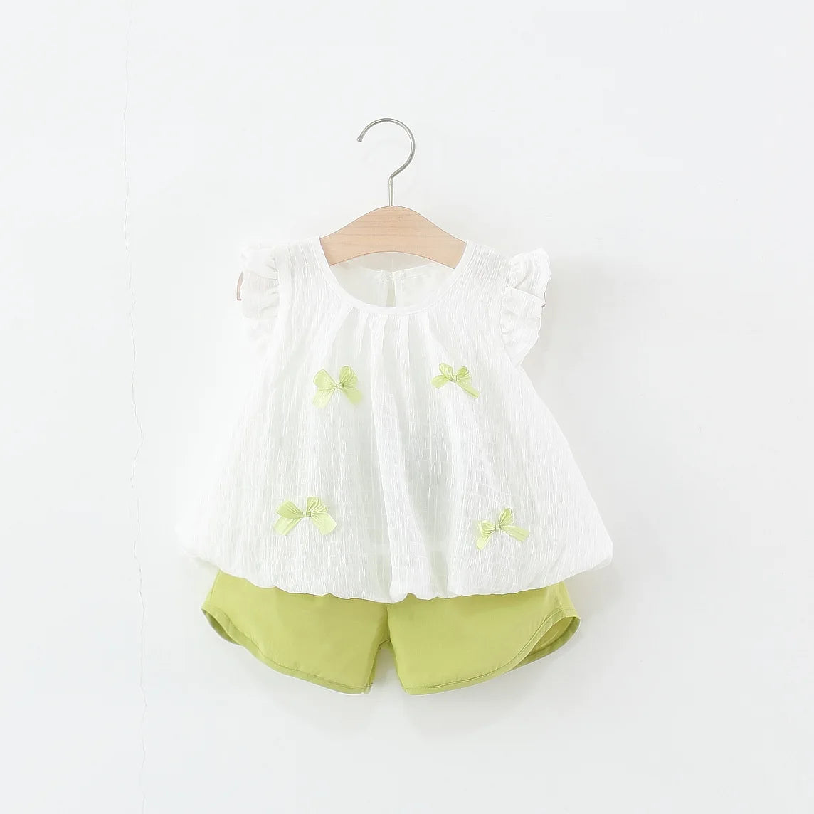 White blouse with ruffled sleeves and green shorts on a hanger against a white background