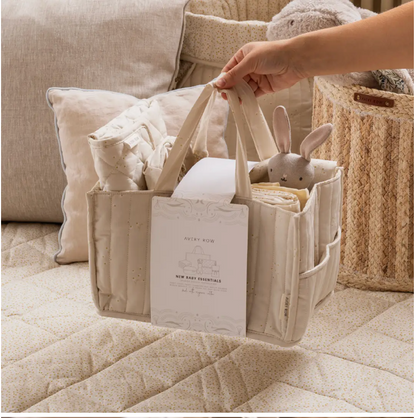 Baby care bag with items including a plush toy, blanket, and diaper on a soft surface.