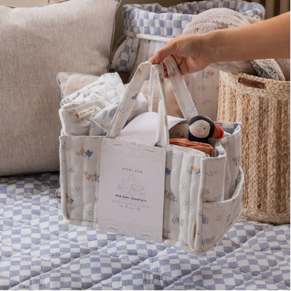 Baby essentials in a fabric storage bag on a checkered blanket with a couch in the background