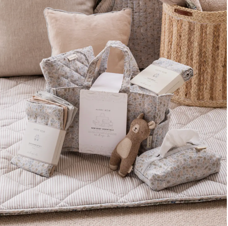 Baby essentials including blankets, books, and a plush toy on a quilted surface.