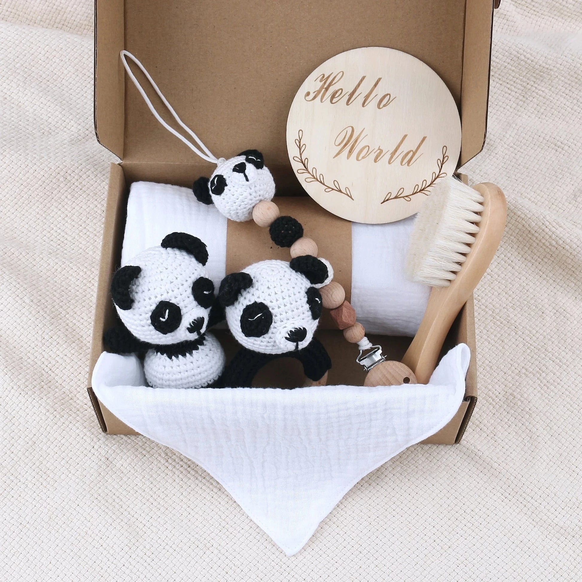 Baby care items including panda toys, a wooden rattle, and a brush in a box on a beige blanket.