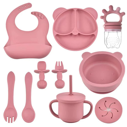 Pink baby dining set including bib, plate, bowl, cup, and utensils on a white background