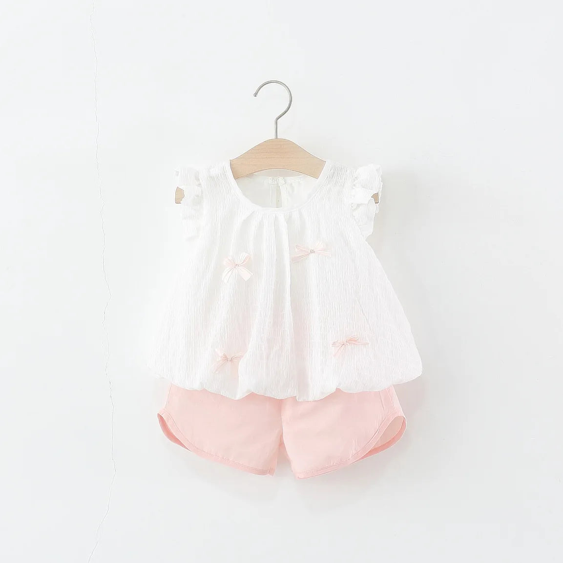 White blouse with ruffled sleeves and Pink shorts on a hanger against a white background