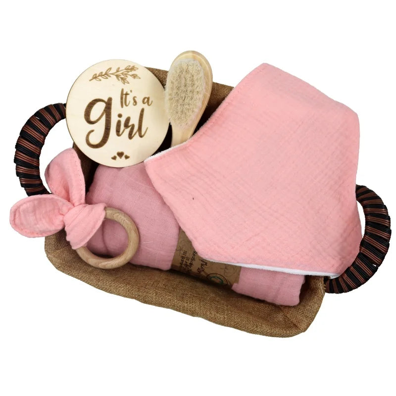 Pink Baby care set with a wooden plaque, brush, Teether and blanket in a woven basket on a white background