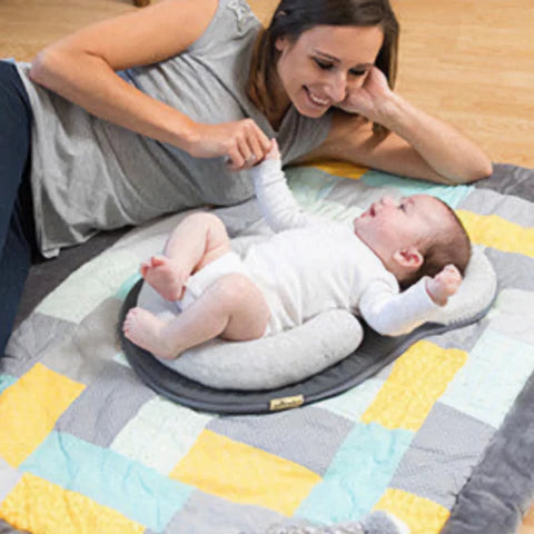 Woman lying on a colorful blanket with a baby on a cushion