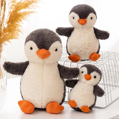 Three plush penguins of different sizes on a white surface with a decorative background.