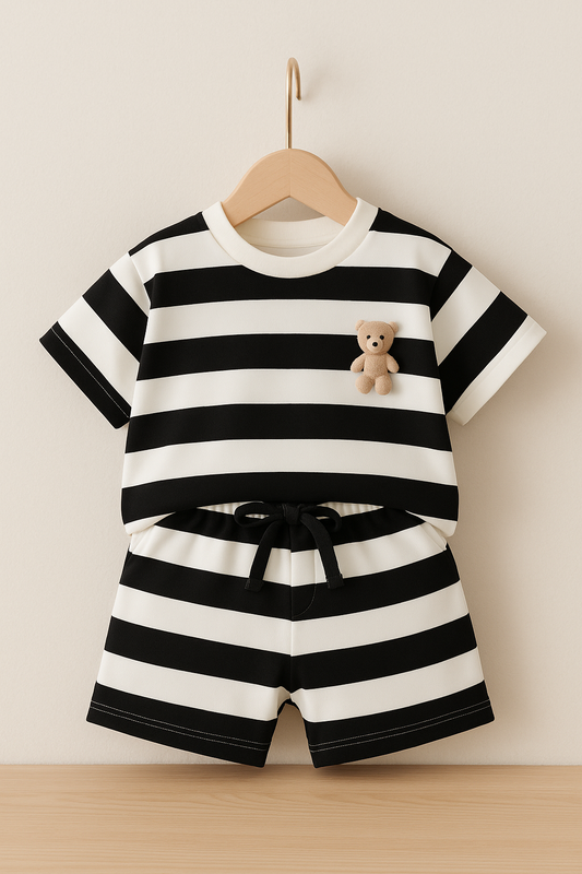 Black and white striped outfit with a teddy bear on a wooden hanger against a beige wall.