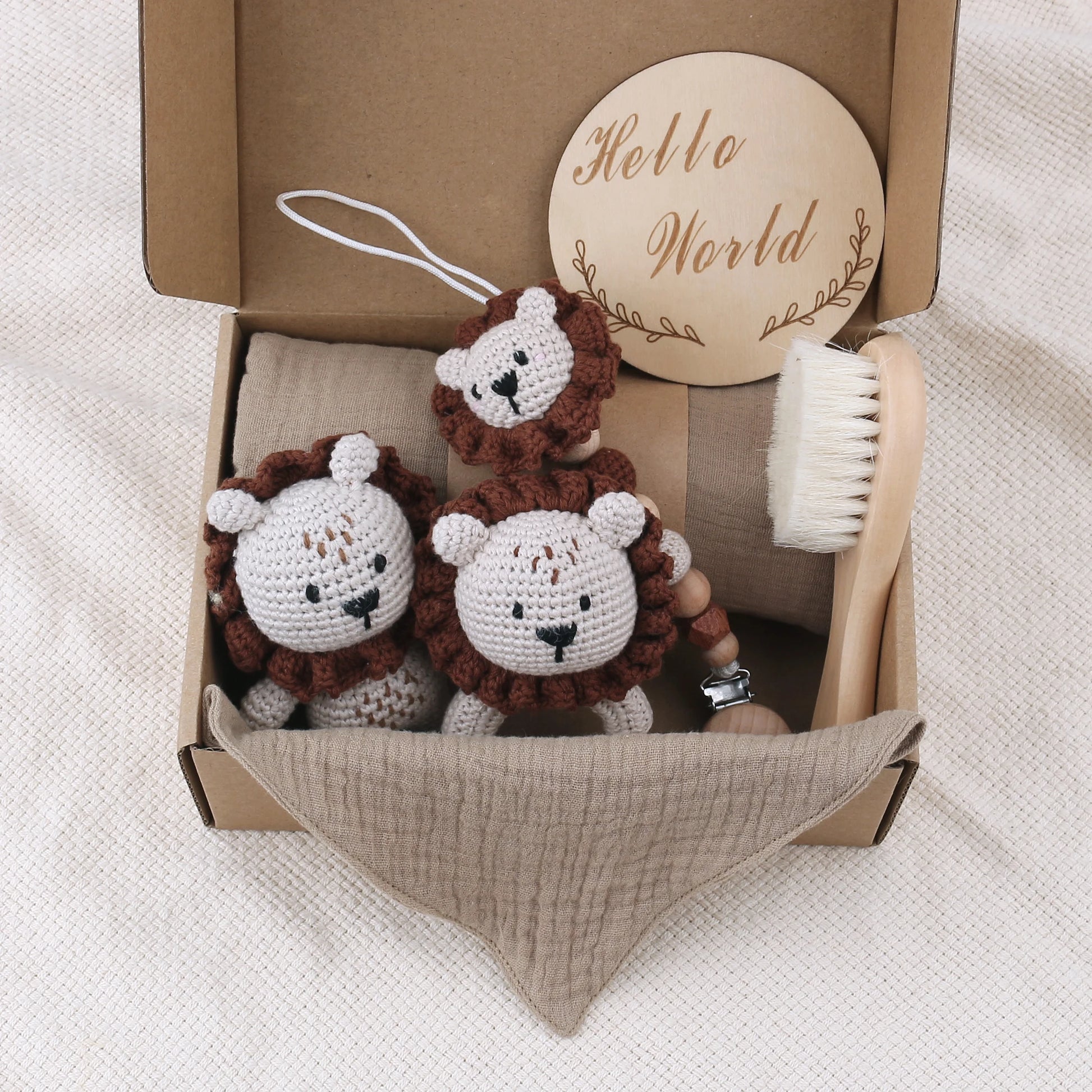 Crocheted teddy bear rattle, baby brush, and 'Hello World' sign in a box on a textured surface.