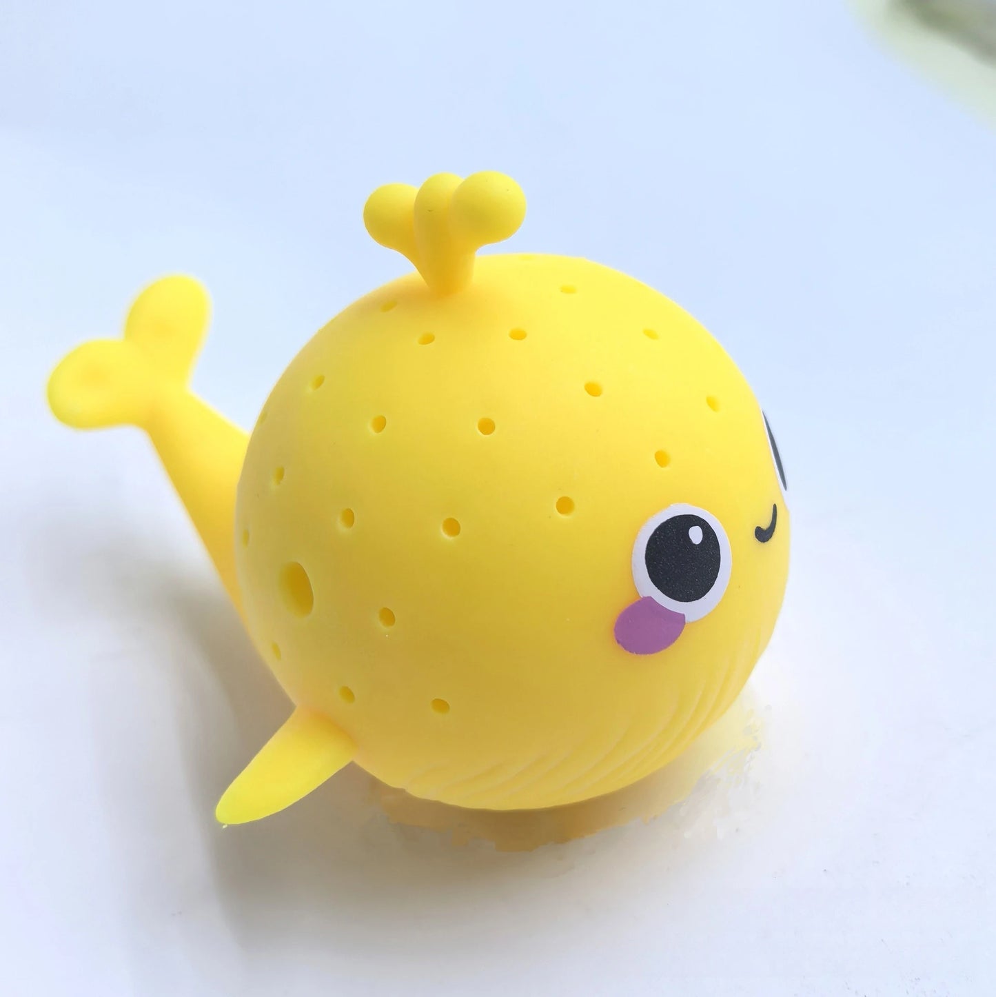 Yellow whale-shaped bath toy with a happy expression on a light blue background