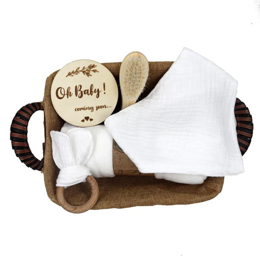 White Baby care set with a wooden plaque, brush, Teether and blanket in a woven basket on a white background