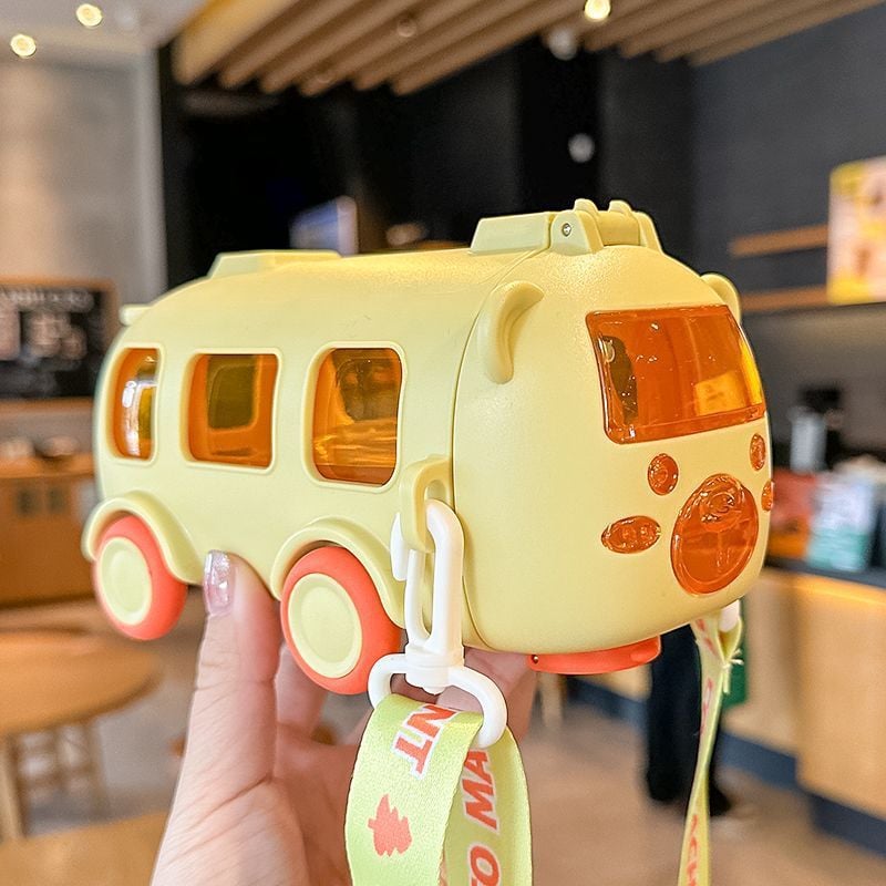 Yellow water bottle & toy bus held by a hand in an indoor setting