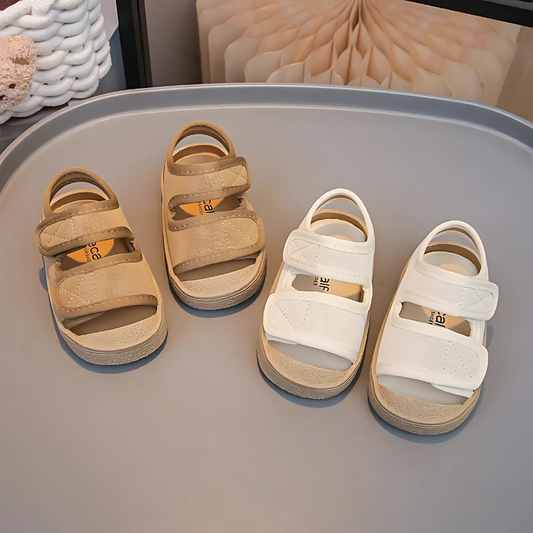 Pair of beige sandals and a pair of white sandals on a gray surface.