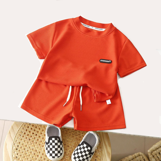 Orange t-shirt and shorts set with a camera and hat on a white surface