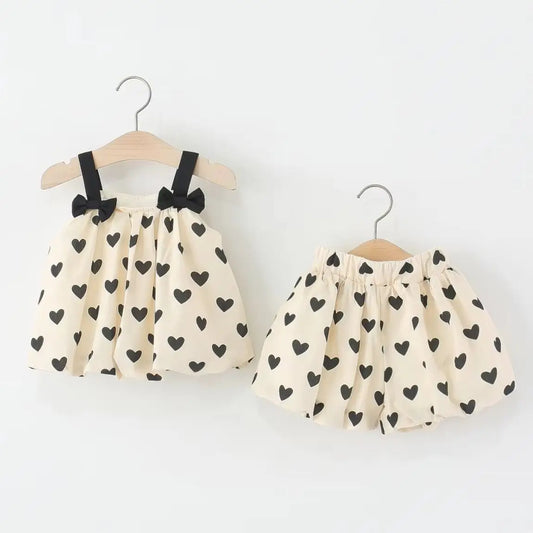 Two children's outfits with heart patterns on hangers against a white background