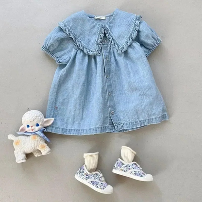 Blue denim dress with ruffled collar, floral shoes, and a plush toy on a neutral background