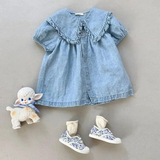 Blue denim dress with ruffled collar, floral shoes, and a plush toy on a neutral background